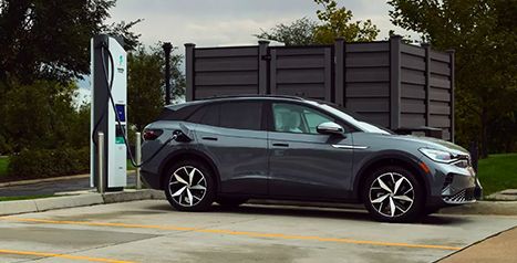 A dark gray Volkswagen ID.4 electric SUV is plugged into an outdoor public fast-charging station.