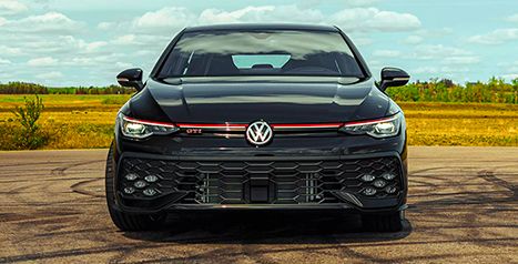 Front view of a black Volkswagen Golf GTI parked on asphalt, highlighting the honeycomb grille and the red stripe.