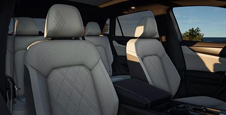Interior view showing the front and second-row seats of a vehicle, upholstered in light grey leather or leatherette with a quilted pattern.