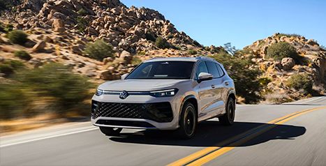 Light grey Volkswagen SUV (Tayron or similar) driving on a winding road in a desert or mountainous environment.