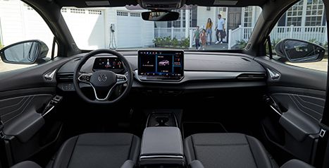 Interior view of a Volkswagen ID.4 showing the dashboard, steering wheel, and touchscreen, with a family walking in front of a house in the background.