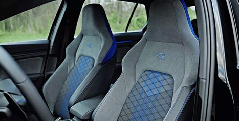 Interior view showing the sport seats of a Volkswagen Golf R with blue and gray cloth upholstery and the embroidered R logo.