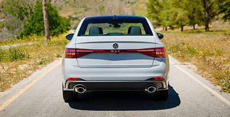 Rear view of a white Volkswagen Jetta GLI sedan with dual exhaust, parked on a rural road.