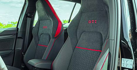 Close-up of the Golf GTI's front sport seats, featuring the embroidered "GTI" logo and red contrast stitching.