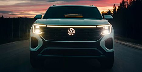Front view of a Volkswagen Atlas or Atlas Cross Sport at night or twilight, highlighting the full-width front LED light bar and headlights.