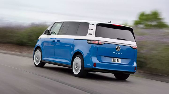 Rear view of a two-tone blue and white Volkswagen ID. Buzz electric van driving on a country road.