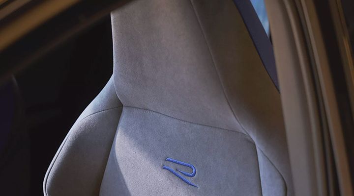 Close-up of the Alcantara upholstery of a performance seat, with the embroidered blue R logo.