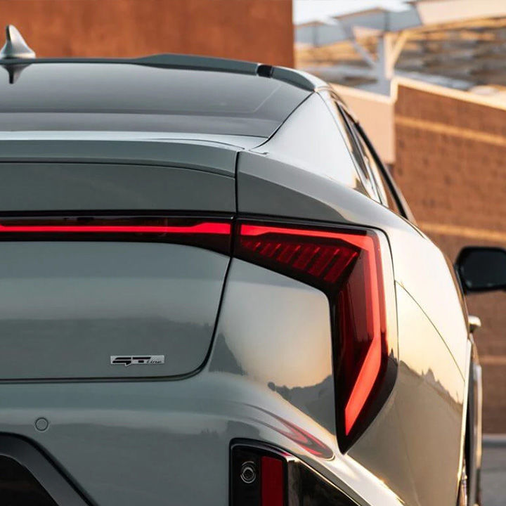 A close-up of the illuminated, curved LED tail light on the rear of a grey Kia .