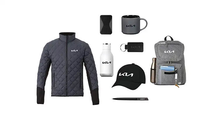 A collection of Kia-branded promotional items, including a quilted jacket, a backpack, a hat, a water bottle, a mug, and other accessories.