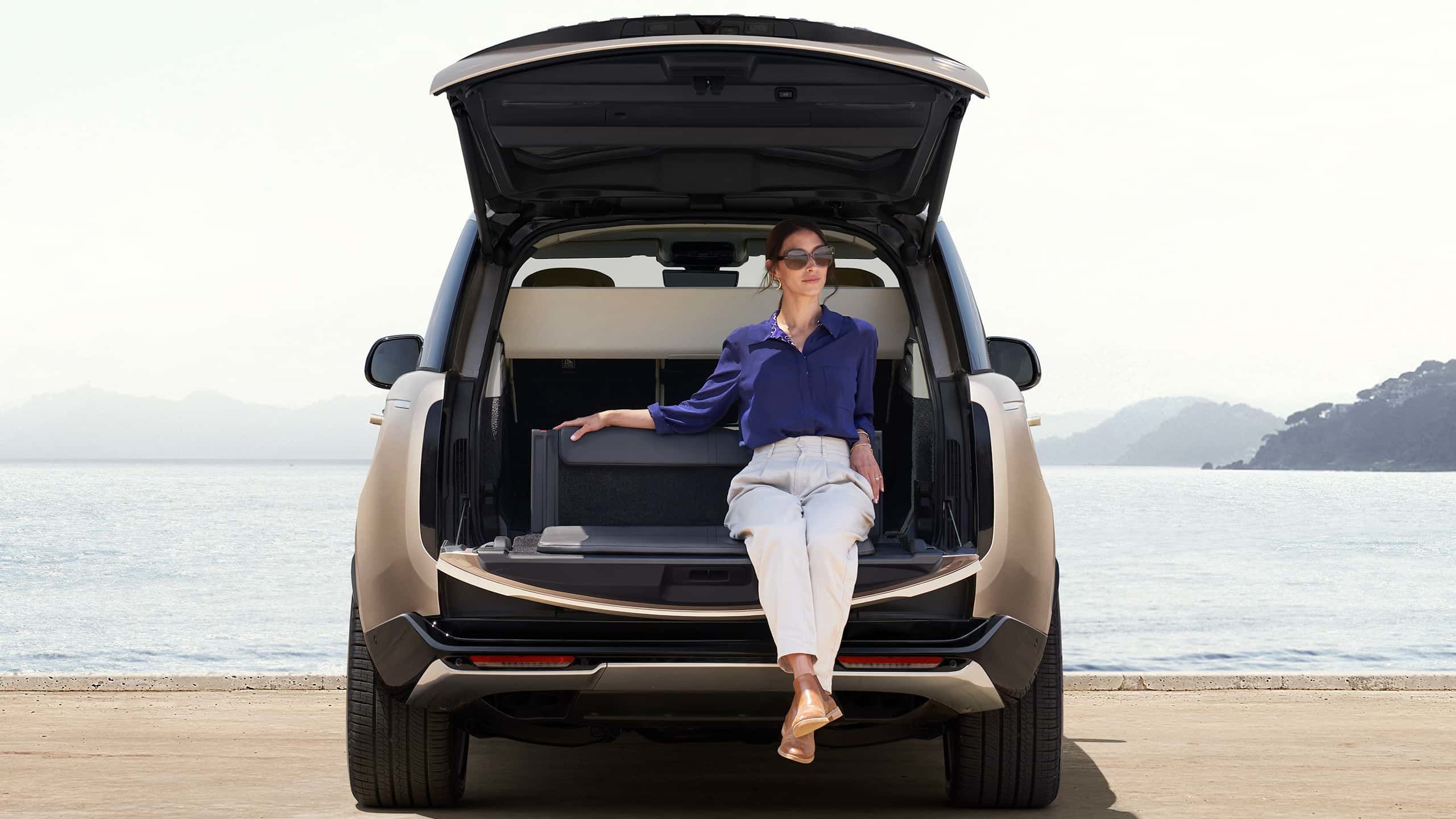 Woman sitting in the open trunk of a Range Rover overlooking the ocean.