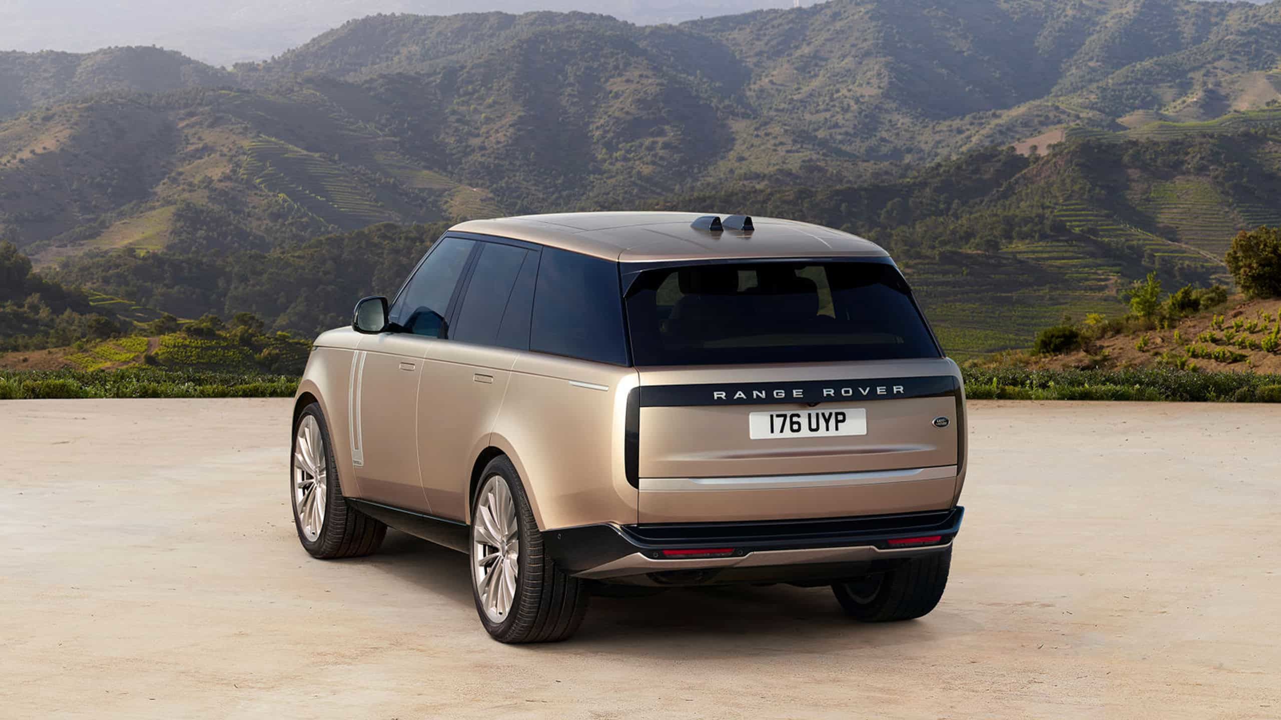 Rear three-quarter view of a bronze Range Rover parked in front of a mountainous landscape.
