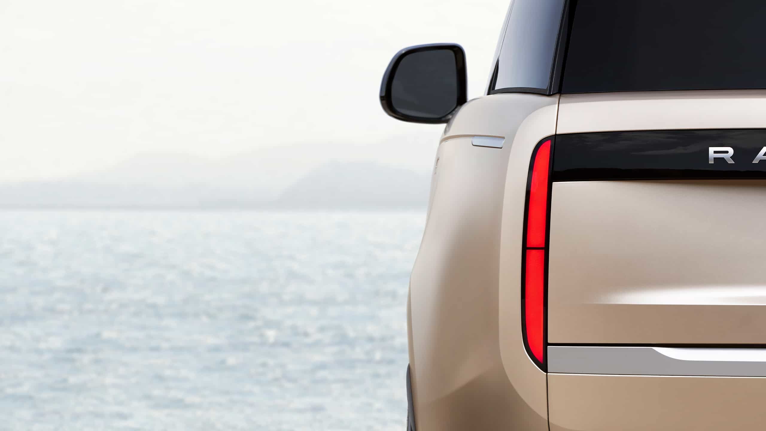 Close-up of the vertical red taillight and Range Rover branding with a sea background.