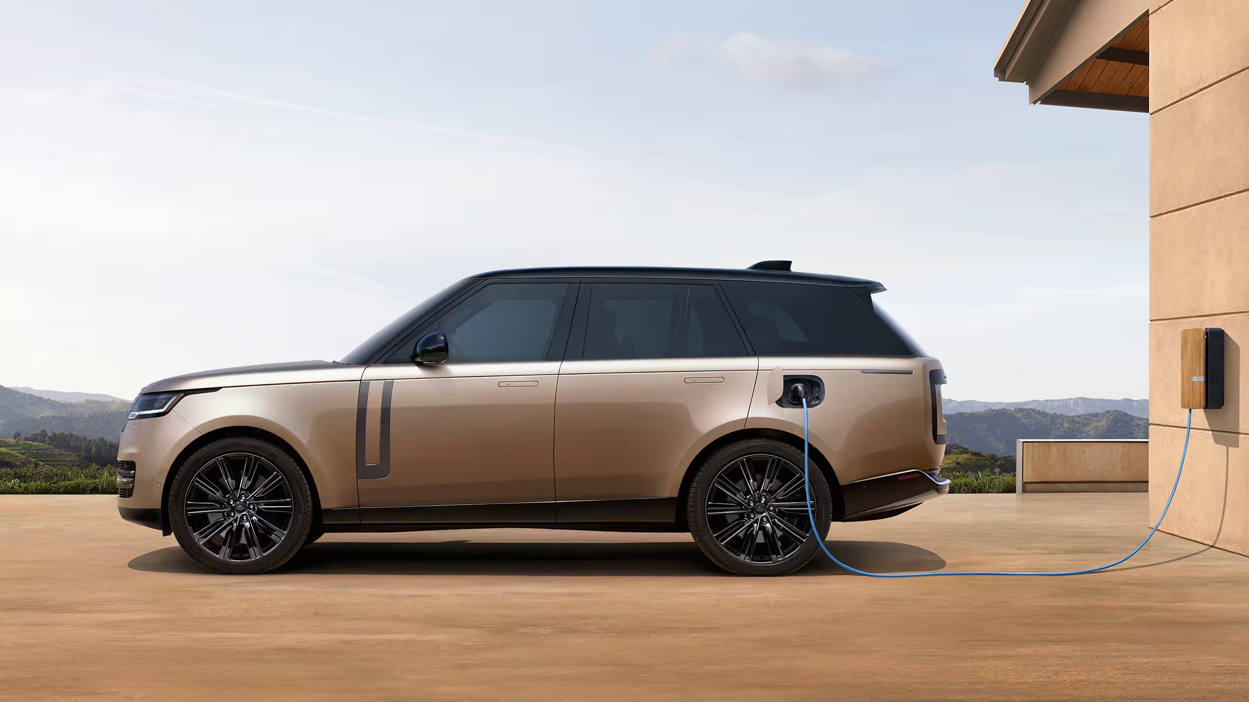 Full profile of a bronze Range Rover plugged into a wall-mounted charging station.