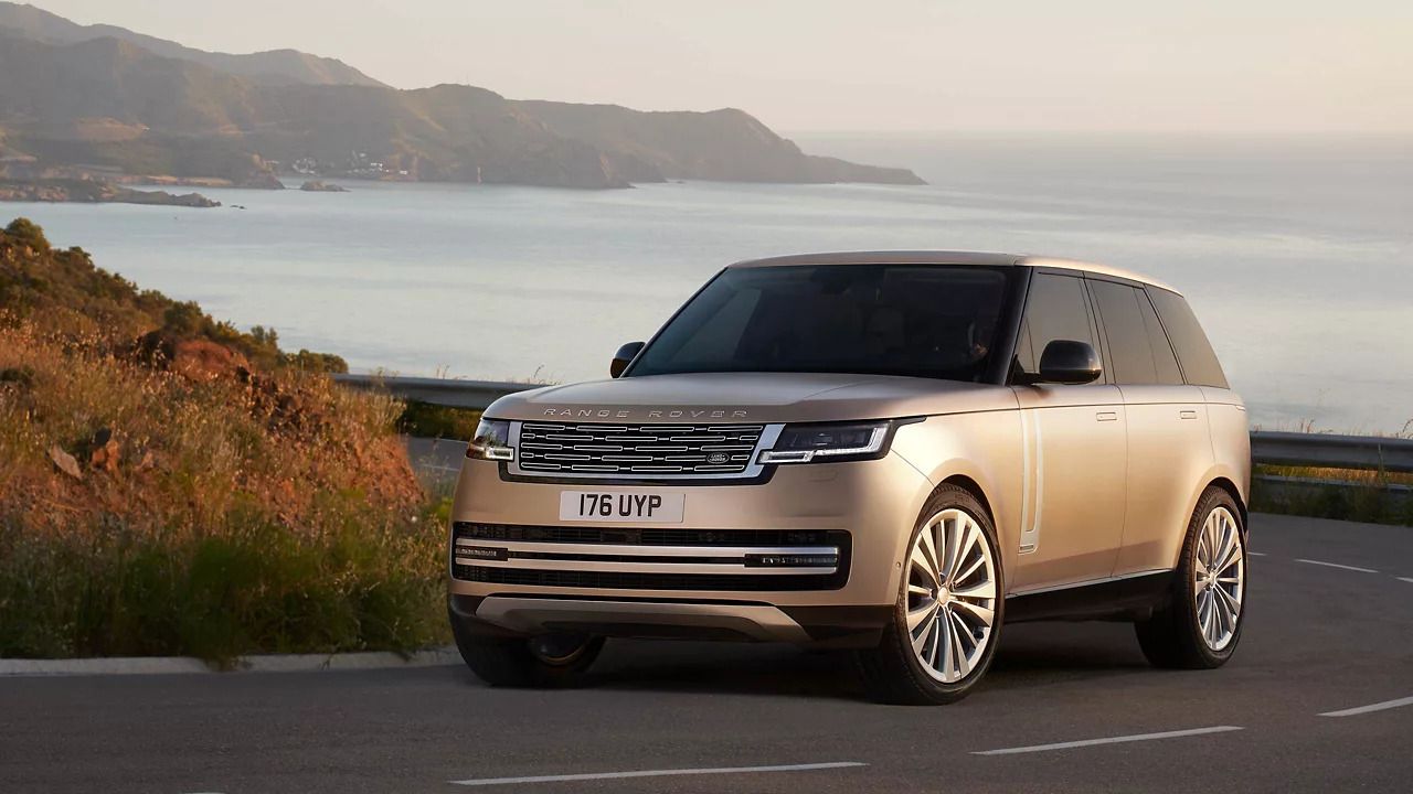 Front view of a bronze Range Rover parked on a coastal road at sunset.