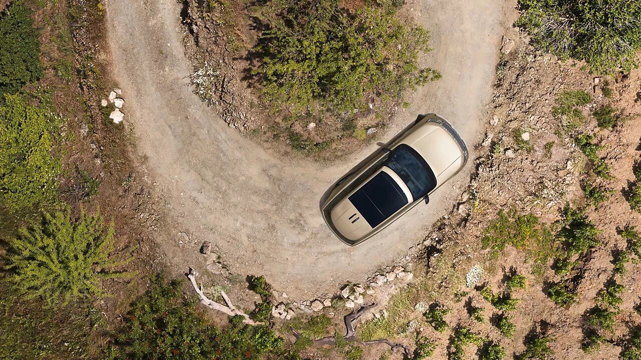 Top-down view of a bronze Range Rover navigating a sharp turn on a dirt road.