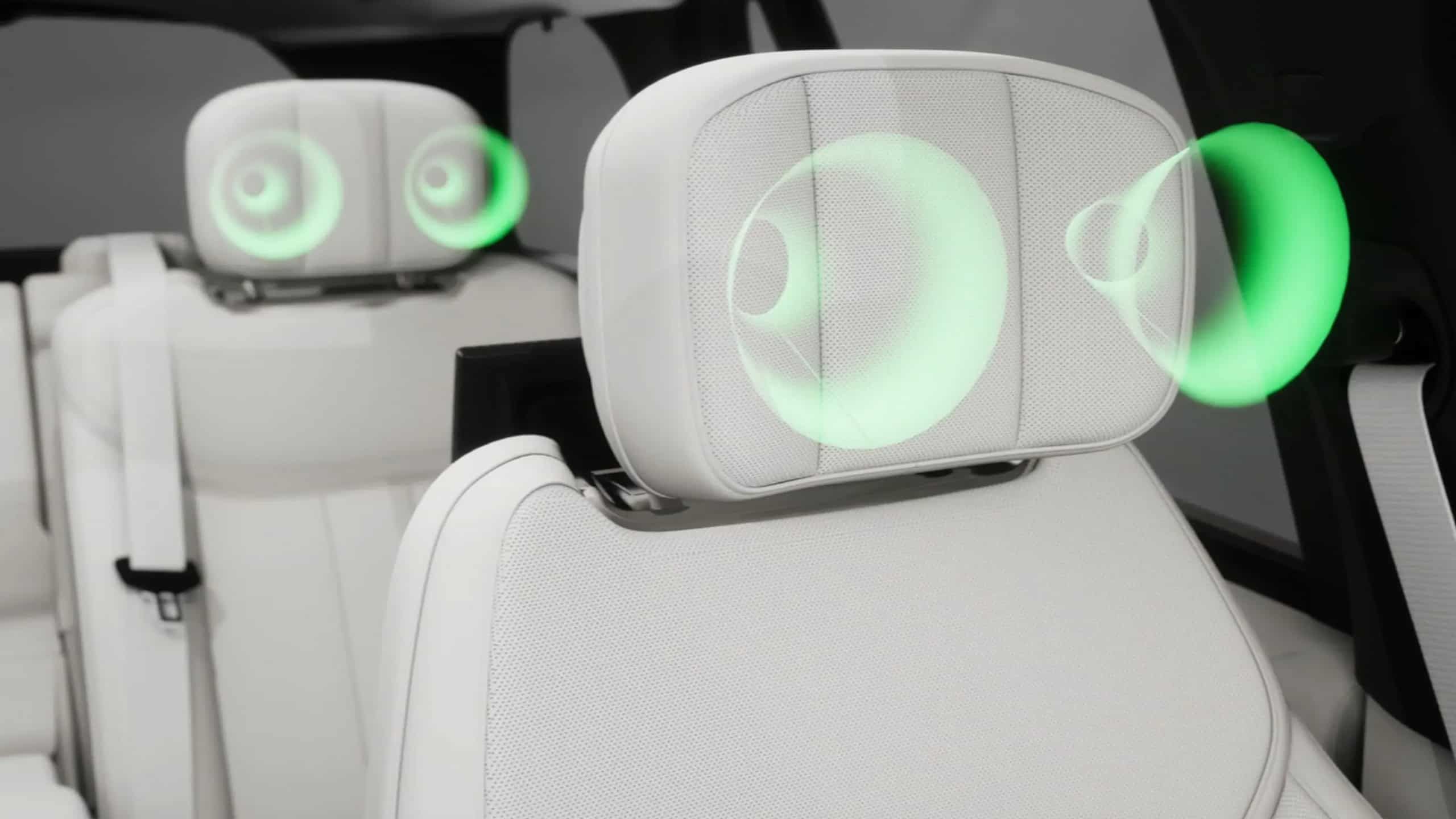 Close-up of white leather headrests with integrated speakers (illustrated by green sound waves).