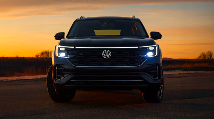 Front view of a black Volkswagen Atlas SUV, with its headlights and LED light bar illuminated at sunset.