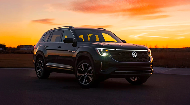 A black Volkswagen Atlas SUV is parked outdoors at sunset, with its headlights and LED light bar illuminated.