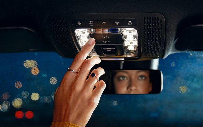 Close-up of a female driver's hand pressing a button on the overhead console inside a car at night.