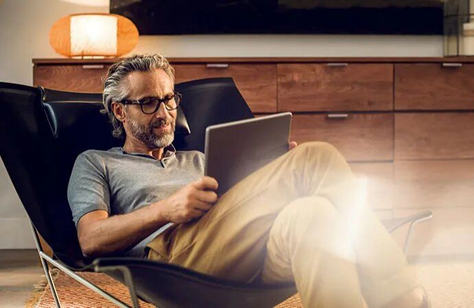 Man with glasses browsing a tablet while relaxing in a chair at home