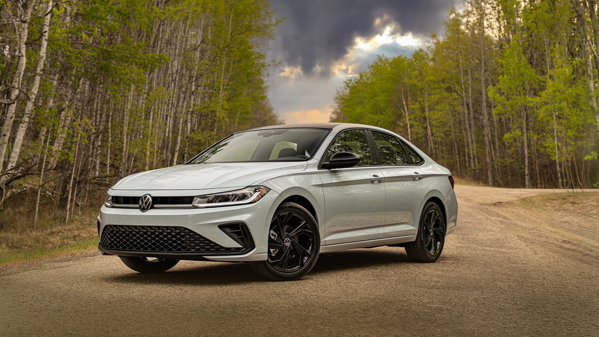 2027 Volkswagen Jetta in Reflex Silver Metallic parked on a dirt road surrounded by birch trees