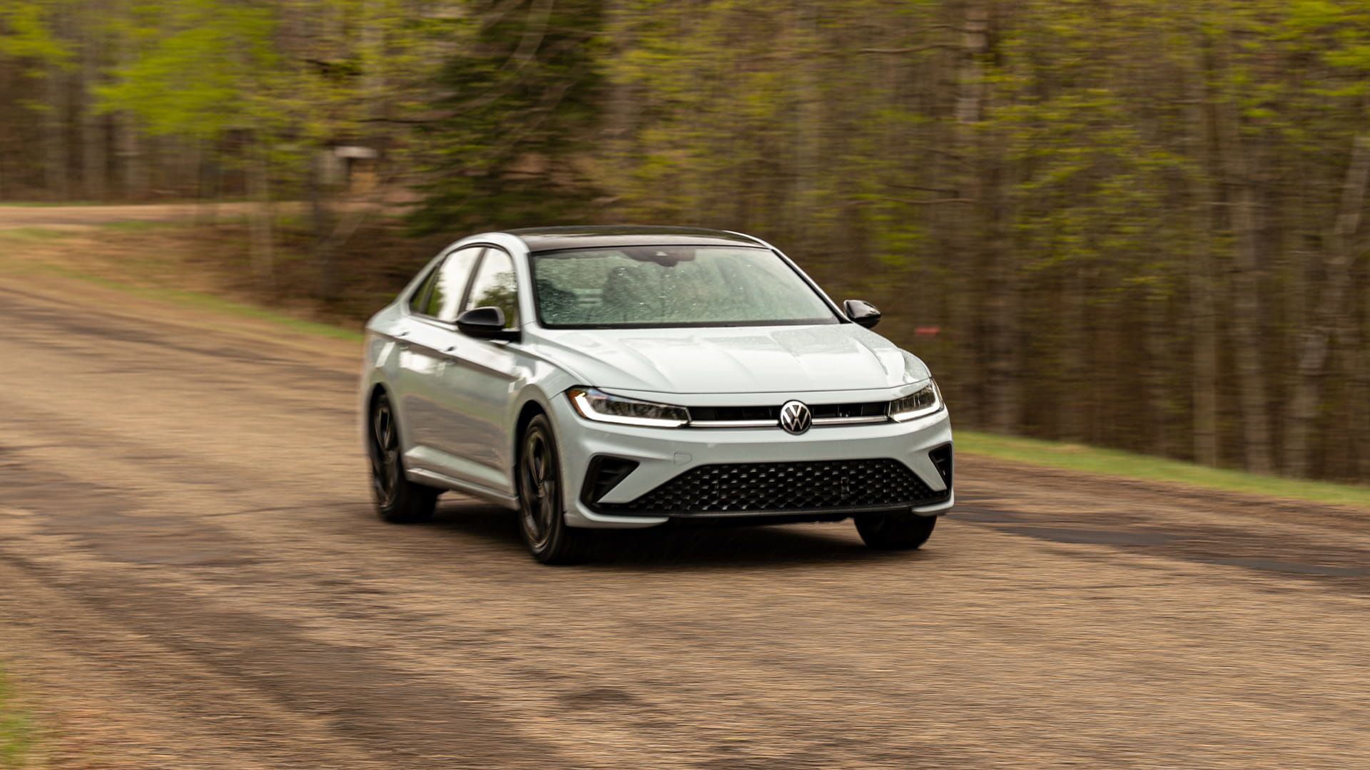 2027 Volkswagen Jetta dynamic front three- quarter view driving on a dirt road surrounded by trees