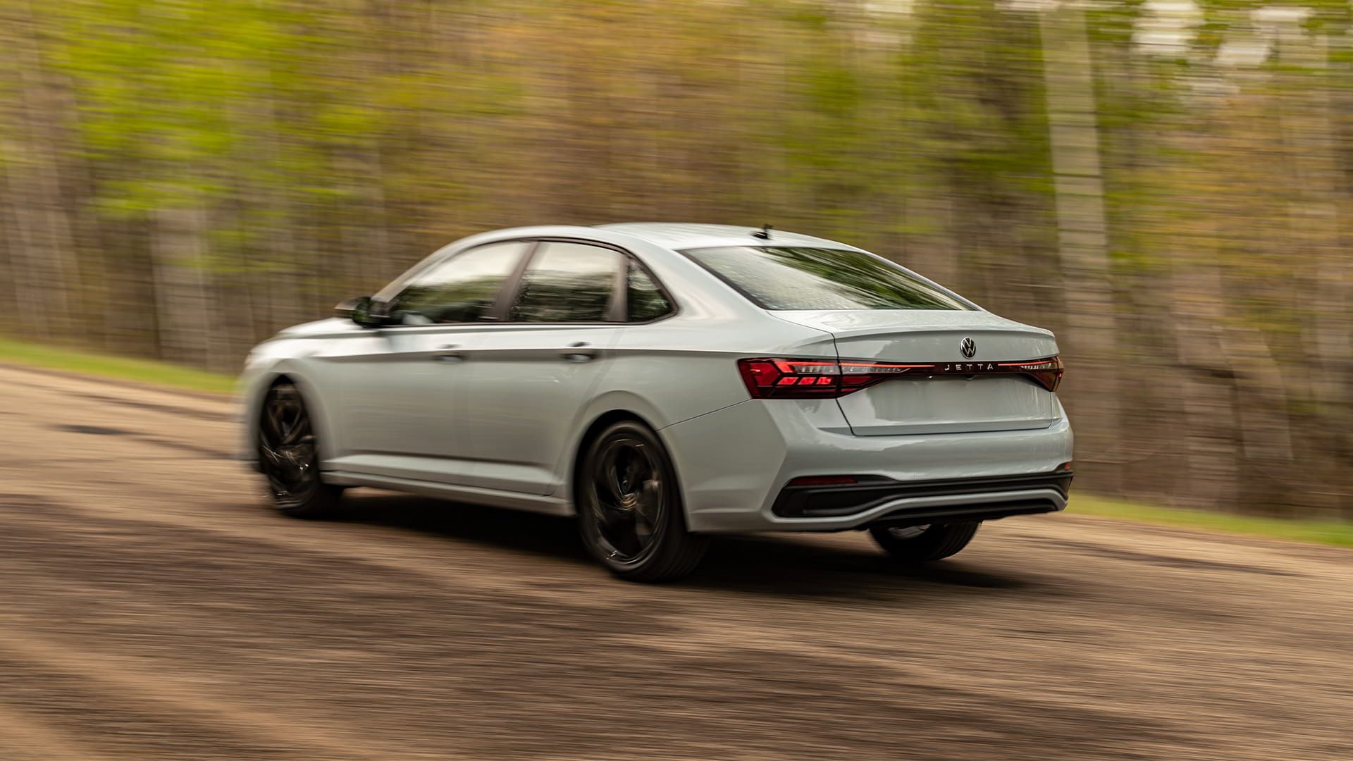 2027 Volkswagen Jetta rear three-quarter view in motion on a rural road in Reflex Silver Metallic