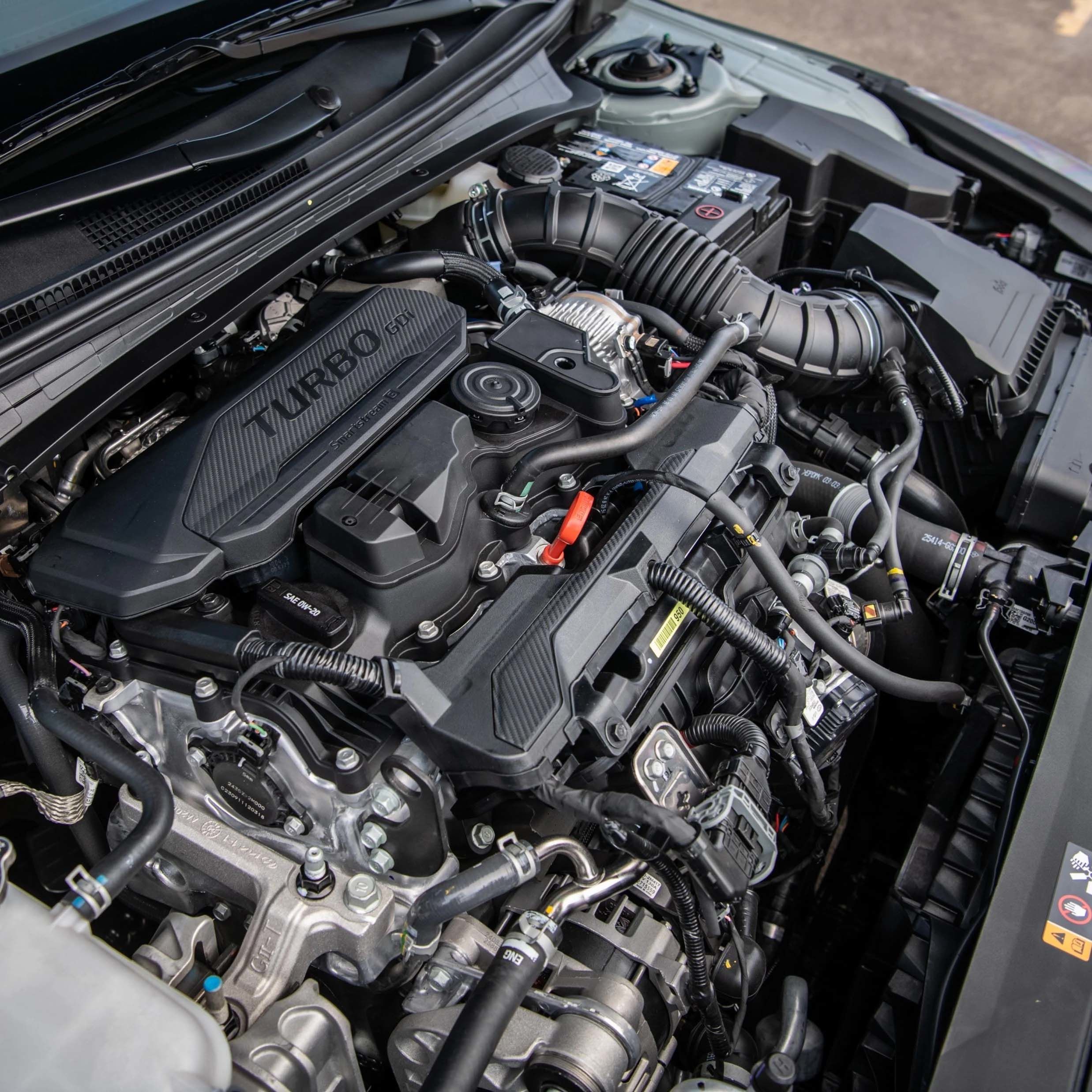 Un gros plan d'un moteur de voiture moderne avec un couvercle noir affichant le mot « TURBO » en lettres stylisées rouges.