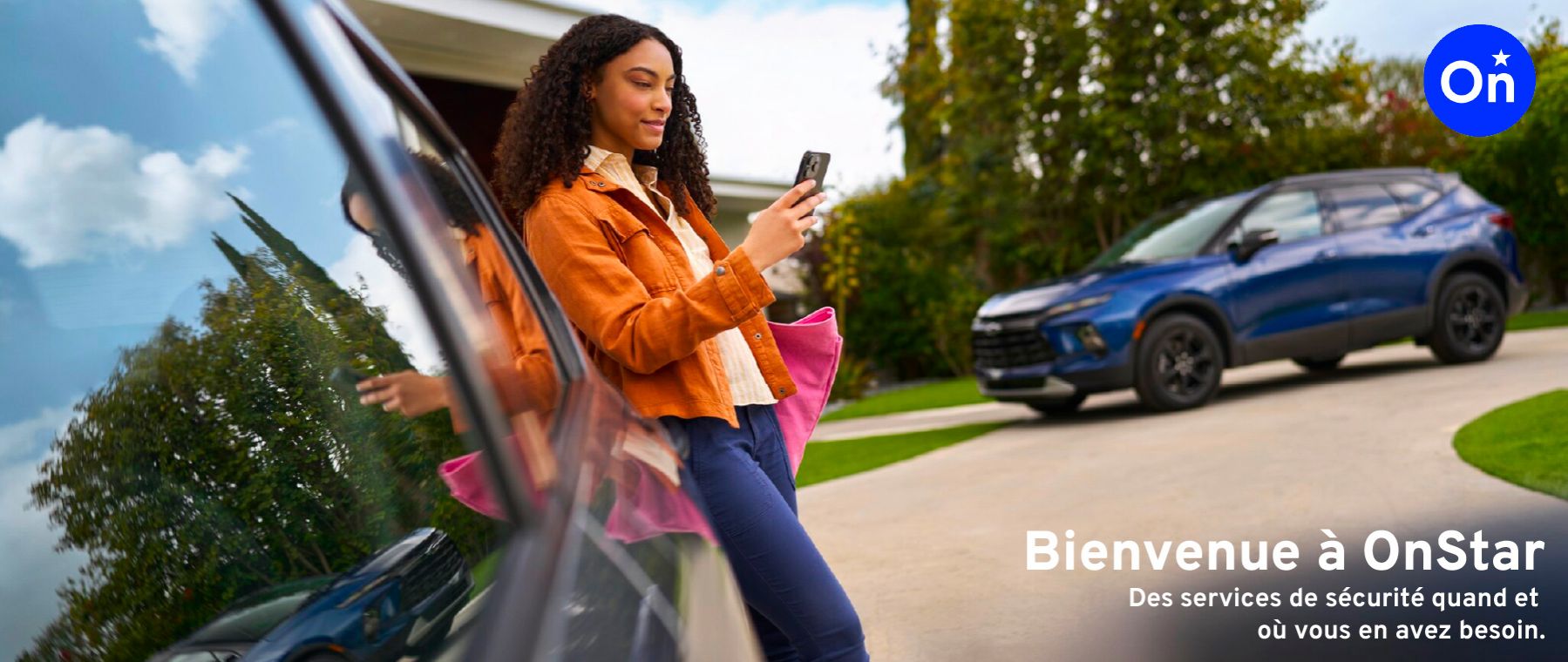 Une femme souriante s'appuie contre la fenêtre de sa voiture (un VUS Chevrolet Blazer bleu) et regarde son téléphone intelligent. Le texte "Bienvenue à OnStar. Des services de sécurité quand et où vous en avez besoin" est affiché.