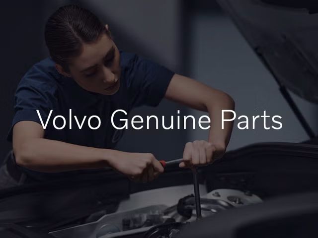 A female technician in a dark blue shirt leans over the open hood of a car, using a wrench on the engine. The text "Volvo Genuine Parts" is overlaid on the image.