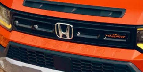 Gros plan de la calandre avant d'un Honda Passport orange, montrant le logo Honda, un insigne « TrailSport » et le nom « PASSPORT » en relief sur le pare-chocs.