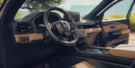 Vue intérieure du Honda Passport depuis le côté conducteur, montrant le volant, le tableau de bord, l'écran numérique et les détails en cuir beige et noir.