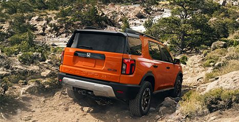 Rear view of an orange Honda Passport driving up a rugged, rocky incline, highlighting the taillights and rear badging.