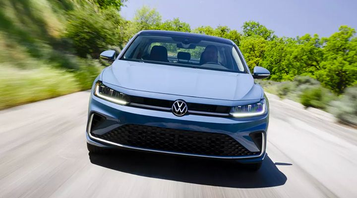 Front view of the blue Volkswagen Jetta driving on a scenic road with greenery on both sides.