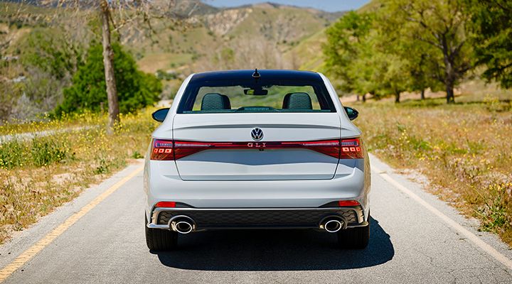 Rear view of a white  Jetta GLI parked on a scenic road with grassy hills in the background.