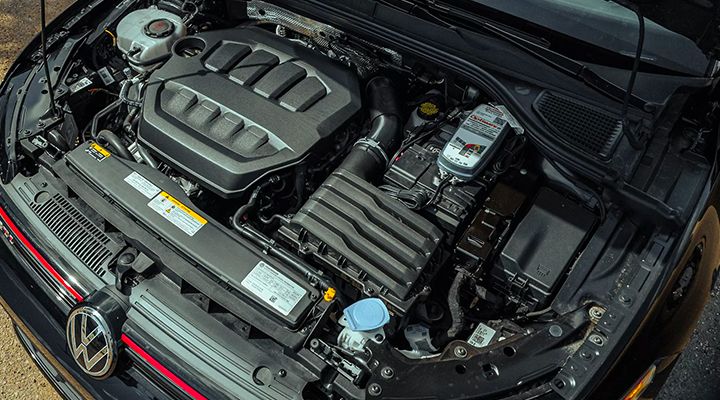 Top-down view of the engine bay of a Volkswagen Golf GTI, showing the engine cover, components, and fluid reservoir.