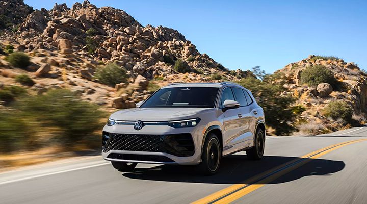 Light grey Volkswagen Tiguan or SUV in motion on a winding road in a desert or mountainous environment.