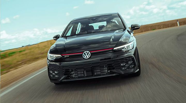 Black Volkswagen Golf GTI, low-angle front view, driving at speed on a winding country road.