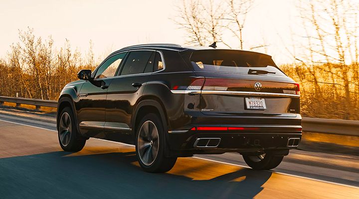 Black Volkswagen Atlas Cross Sport, rear three-quarter view driving on a road, illuminated by the sunset.