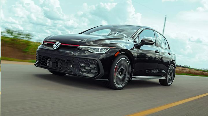 Front three-quarter view of a black Volkswagen Golf GTI driving at speed on a road.