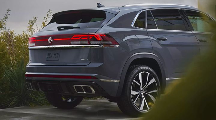 Rear three-quarter view of a dark grey Volkswagen Atlas Cross Sport parked, highlighting the LED taillight bar and dual exhaust tips.