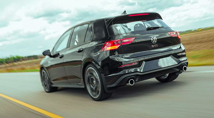 Rear three-quarter view of a black Volkswagen Golf GTI in motion, showing the dual exhaust and taillights.