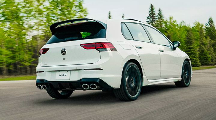 Rear view of a white Volkswagen Golf R driving quickly on a road, highlighting the spoiler and quad exhaust tips.