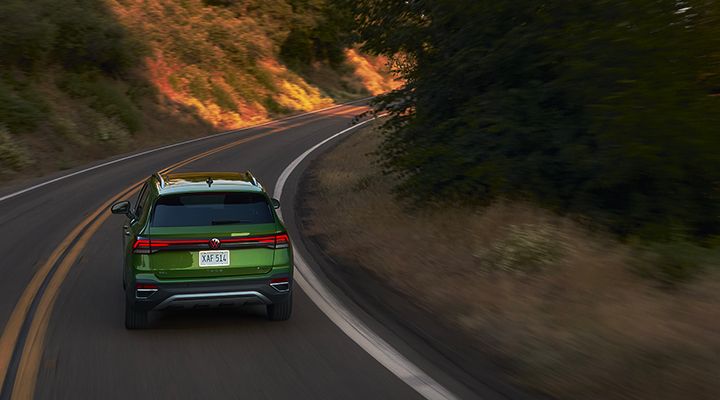 Vue arrière du Volkswagen Taos 2026 vert roulant sur une route sinueuse en forêt.