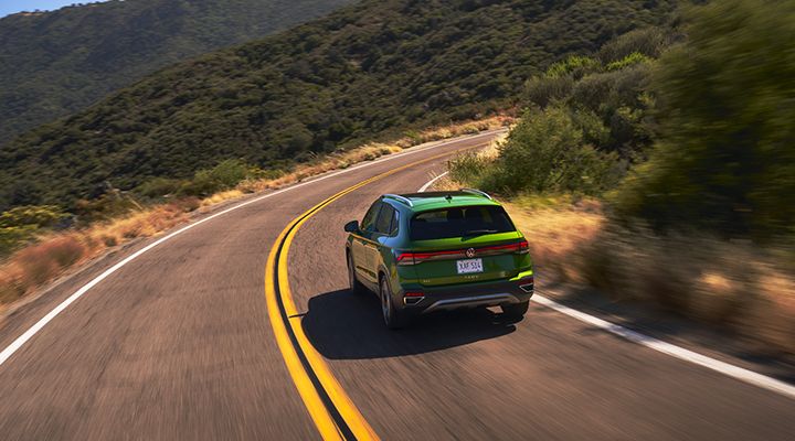 Rear view of the 2026 Volkswagen Taos in green driving through a winding forest road.
