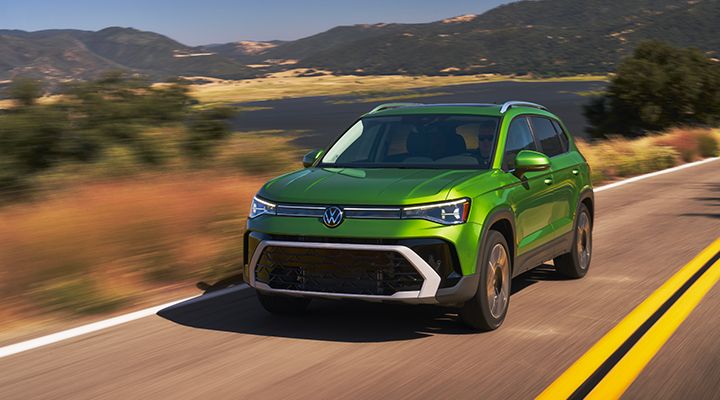 2026 Volkswagen Taos in motion with rolling hills and mountains in the backdrop.