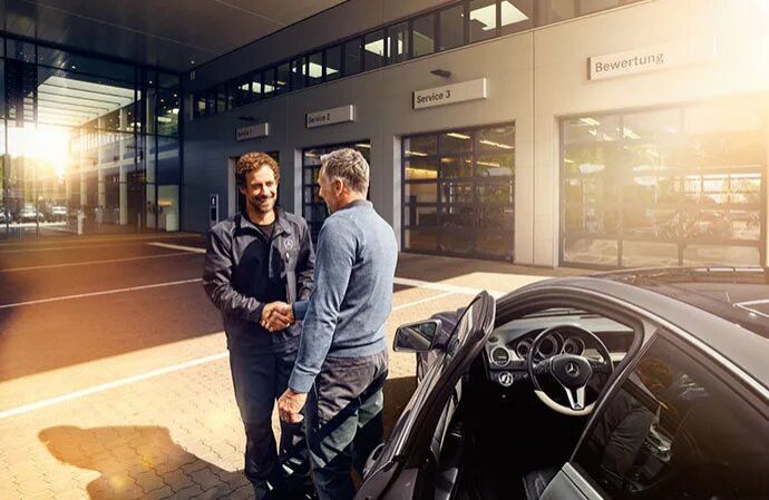 A mechanic shaking hands with a customer outside a Mercedes-Benz service center.