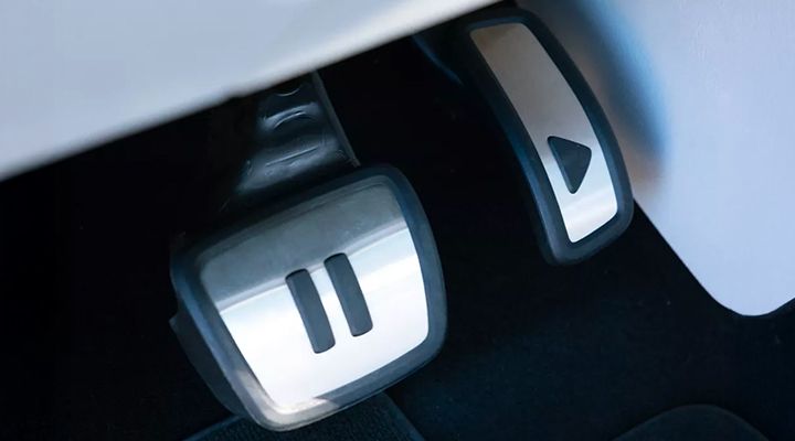 Close-up of a car's pedals, one bearing a "pause" symbol and the other a "play" symbol.