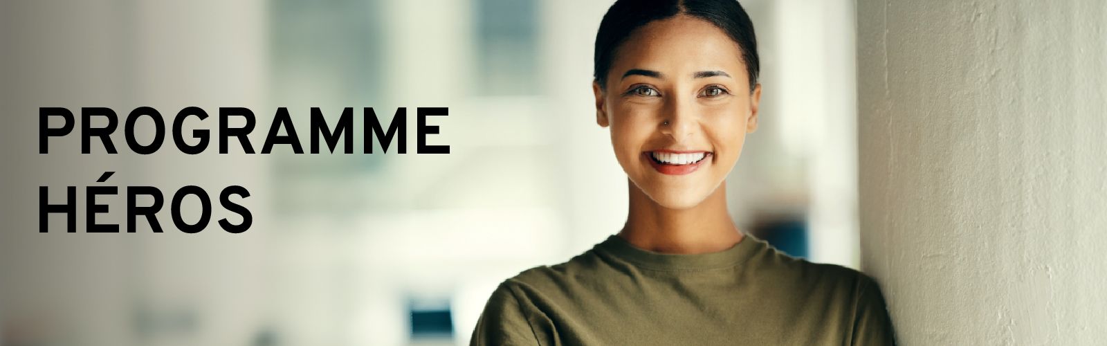 Femme souriante portant un t-shirt de style uniforme militaire ou de service, avec le texte "PROGRAMME HÉROS" superposé.