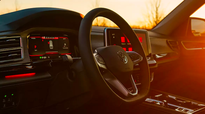 Interior view of an SUV at sunset, showing the steering wheel and digital dashboard, highlighted by red ambient light.